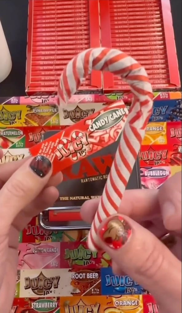 Hands holding Juicy Jay's Candy Cane rolling papers next to a striped candy cane