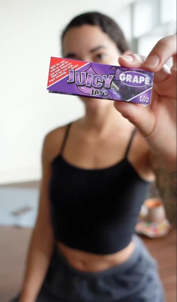 Woman holding a pack of Juicy Jay's Grape rolling papers toward the camera