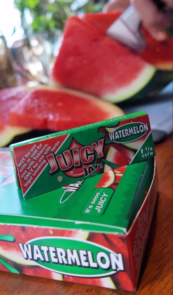 Juicy Jay's Watermelon rolling papers on their box beside sliced watermelon